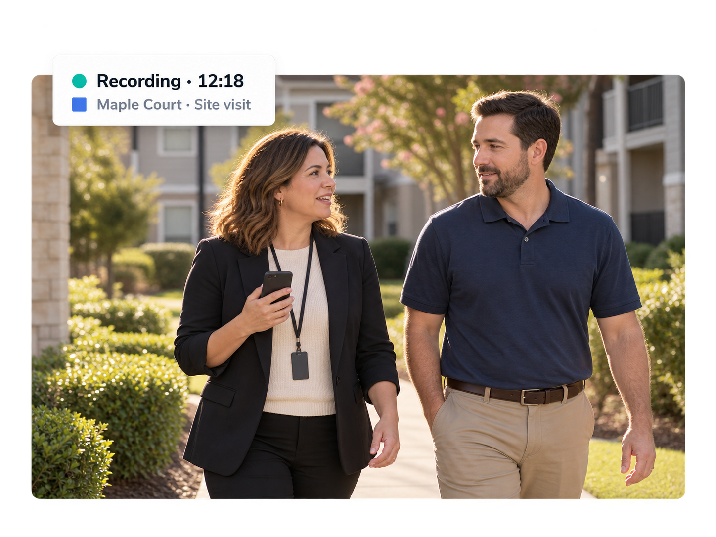 A regional manager and a property manager walking the property side by side, mid-conversation, with the phone quietly recording